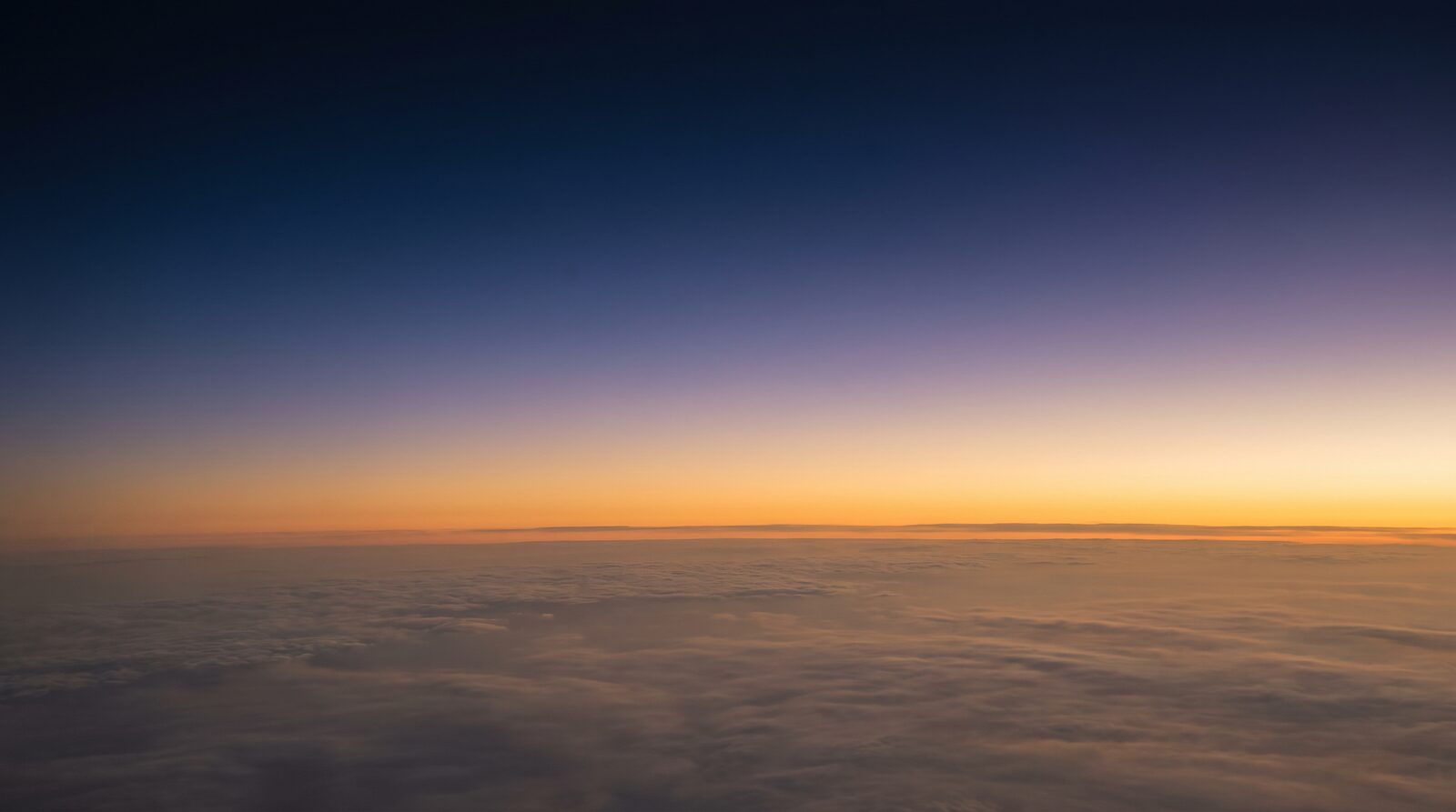 Gradient sky at high altitude transitioning from deep navy blue to warm amber near the horizon